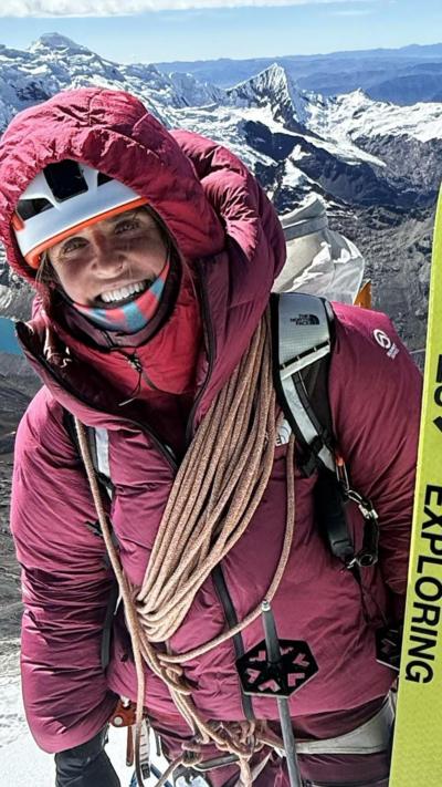 Fay manners pictured in Peru wearing a heavy purple ski coat ad holding two bright yellow skis.