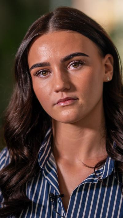 A young woman with long brown hair looks into the camera with a serious expression 