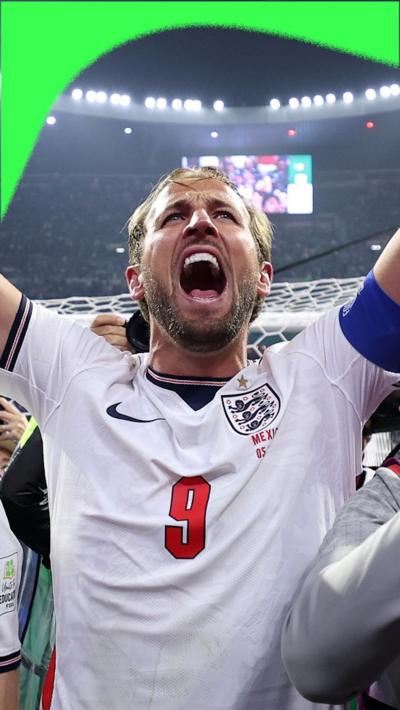 Harry Kane celebrates and sings with his hands in the air wearing his white England playing shirt