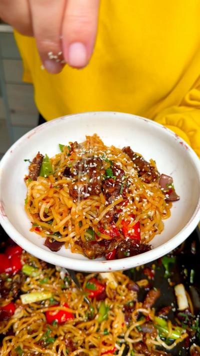 A bowl with beef chilli traybake. A hand is sprinkling sesame seeds on top