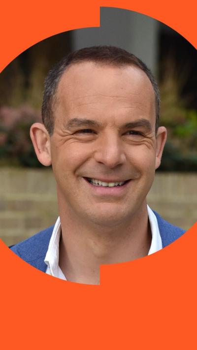 Martin Lewis smiles in the street. He has short brown hair and wears a blue suit jacket with white shirt