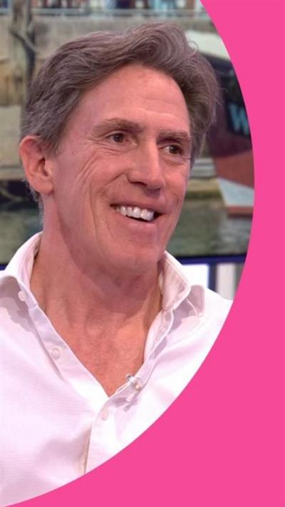 Rob Brydon in a pink shirt sitting and smiling