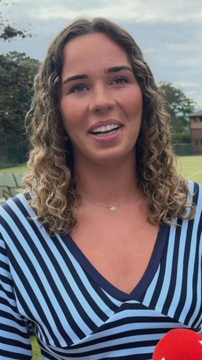 A girl with brown and blonde curly hair smiling. She is wearing a navy and light blue striped top. 