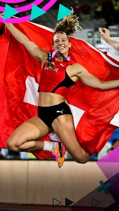 Angelica Moser jumps while holding the Swiss flag behind her back
