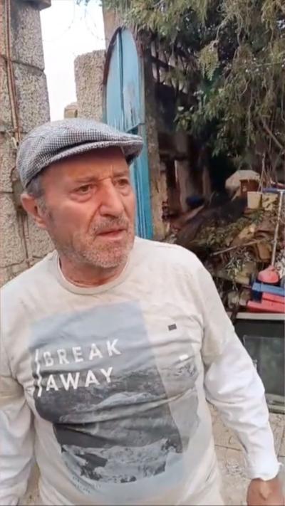 A man in Spain looking upset, wearing a flat cap and standing outside in a courtyard 