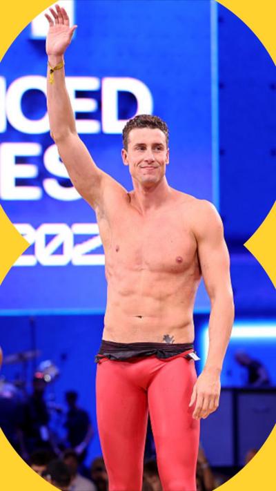 An athlete stands with right arm raised, wearing skintight pink spandex trousers.