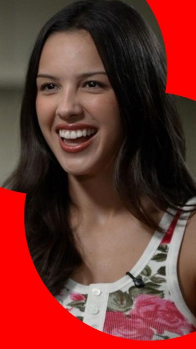 Olivia looks off camera and laughs during an interview