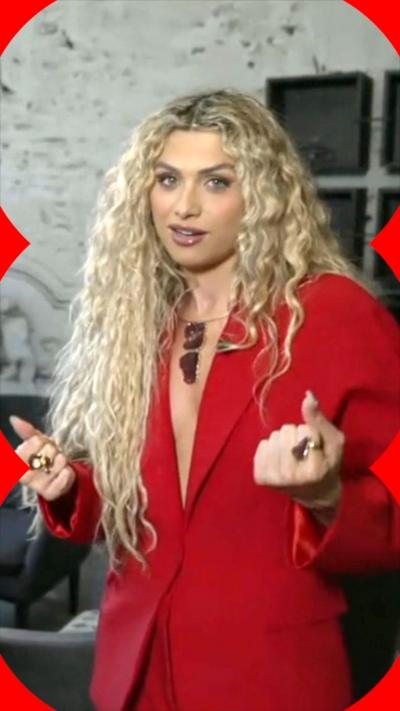 Antigoni Buxton stands and looks at the camera. She wears a red blazer and bunches her fits.