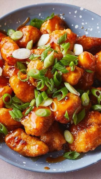 Blue plate with sweet n sour chicken pieces and spring onion sprinkled on top.