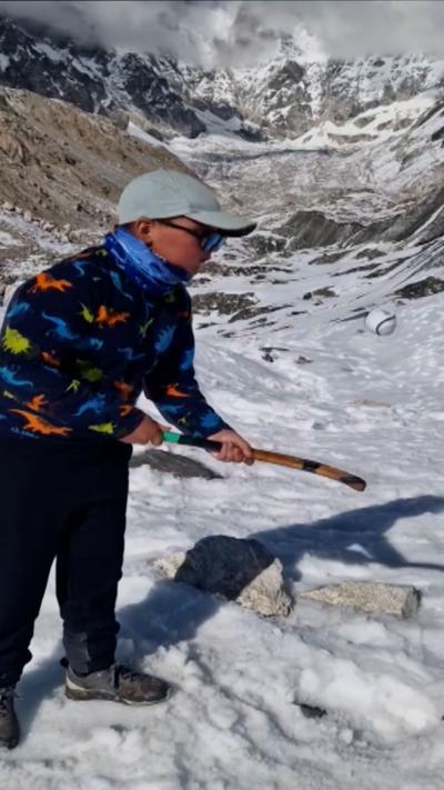 A young boy does keepy-ups with a shinty stick and ball on the slopes of Mount Everest