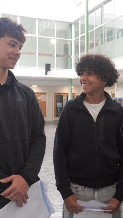 Two boys, both in black tops stand next to each other smiling