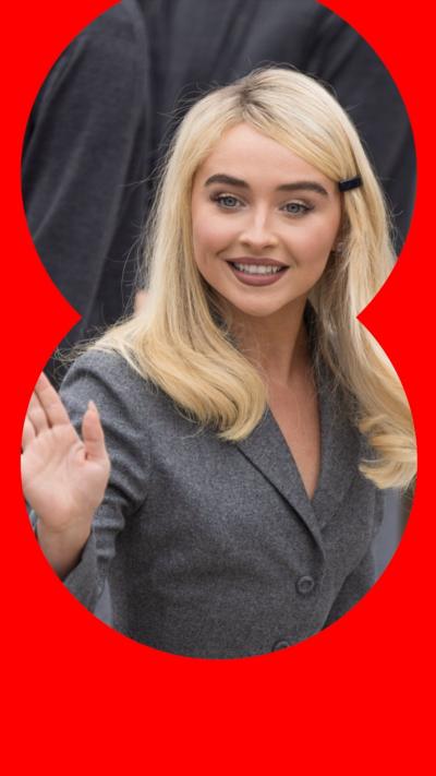 Sabrina Carpenter waving in a grey suit