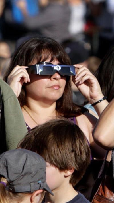 A woman is holding solar eclipse glasses in front of her face. 