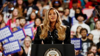 Beyonce at a podium with supporters in the backgrounds 