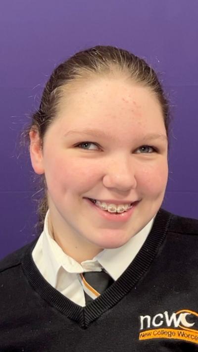 A teenage girl with a black jumper, white shirt and black tie in a purple radio studio