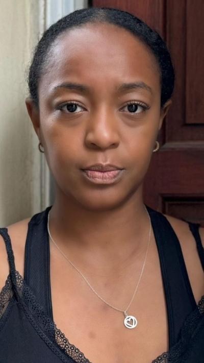 A woman with dark hair pulled back from her face standing in front of a door wearing a silver necklace