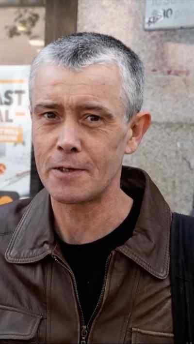 A man with short grey hair and wearing a brown leather jacket