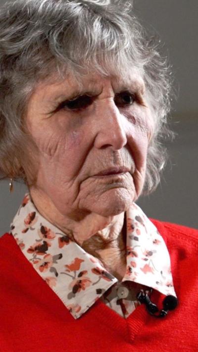 A woman wearing a red cardigan and flowery shirt