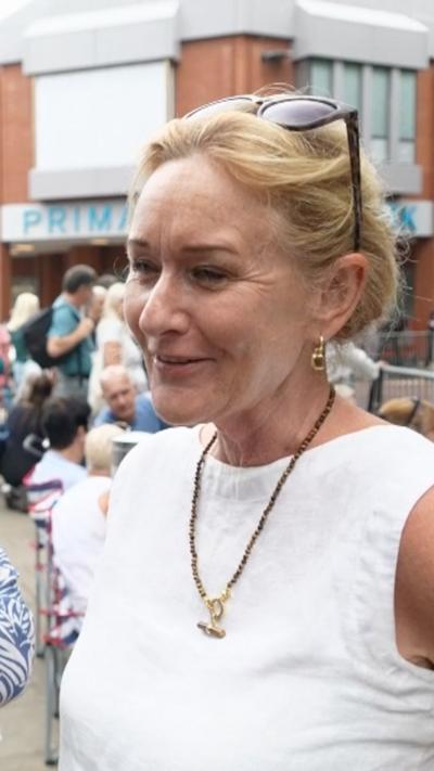 A woman in a white top and blonde hair with sunglasses on her head
