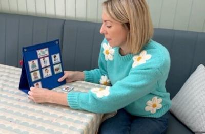 A woman with a turquoise jumper with white and yellow flowers on it looks at a planner on a blue background