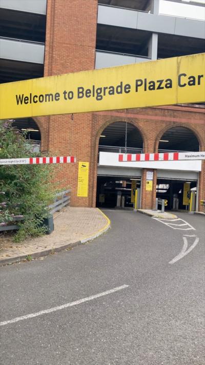 A multi-story car park with brick and glass frontage with the letters N C P on the glass section against the backdrop of a cloudy sky.