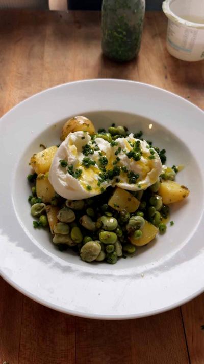 A white bowl on a wooden worksurface filled with potato and veg salad topped with torn mozzarella. 