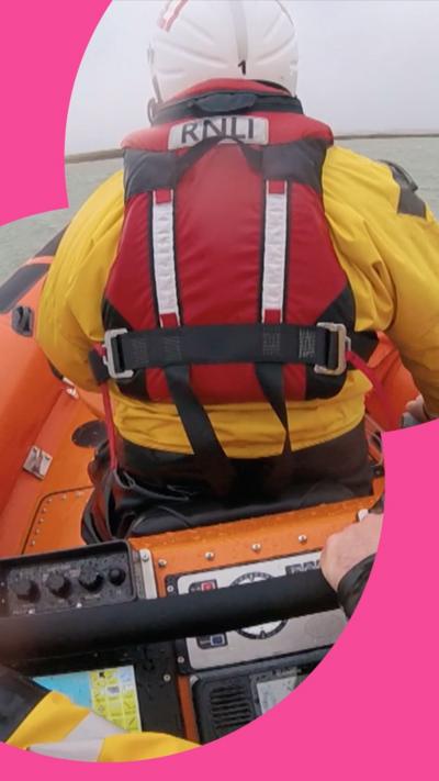 View from behind of a lifeguard in yellow suit and life vest with a white helmet looking out to sea