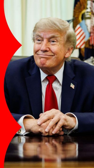 US President Donald Trump smiles while sitting at the Resolute Desk