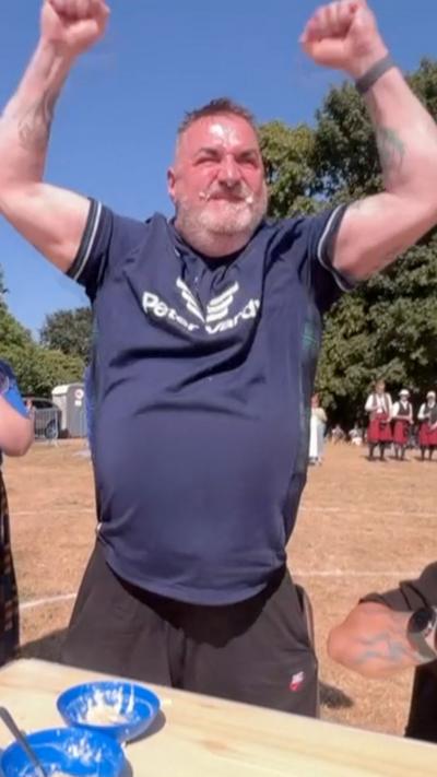 A man in a blue sports shirt raising his arms in the air in a field