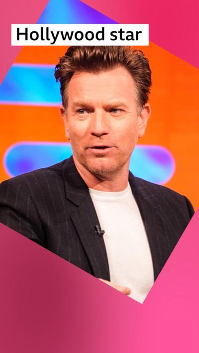 A man, Ewan McGregor, speaks in front of a bright orange background - he has short brown hair and wears a black jacket