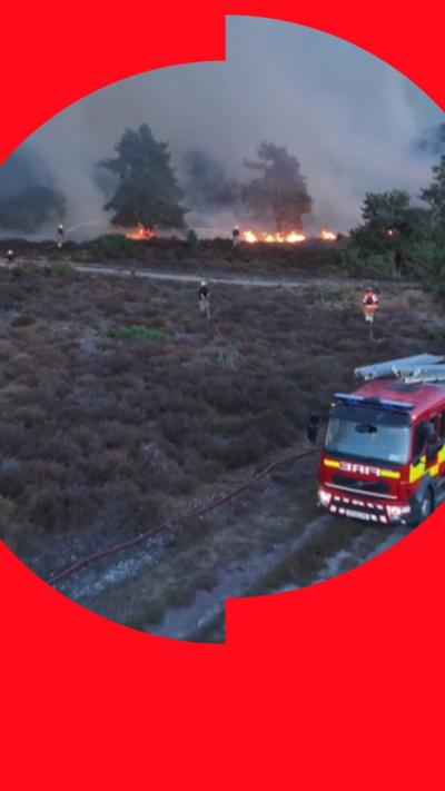 Fire engine at heathland wildfire with firefighters battling flames