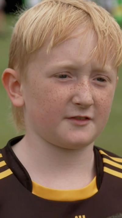 A young boy with blonde hair wearing a black sports top with yellow detailing