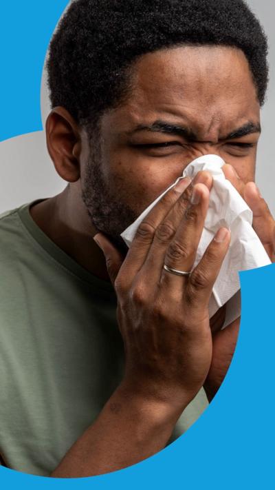 A man sneezes and holds a tissue to his nose