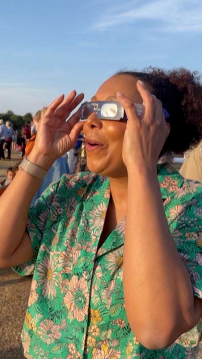 A woman in solar eclipse glasses looks skyward