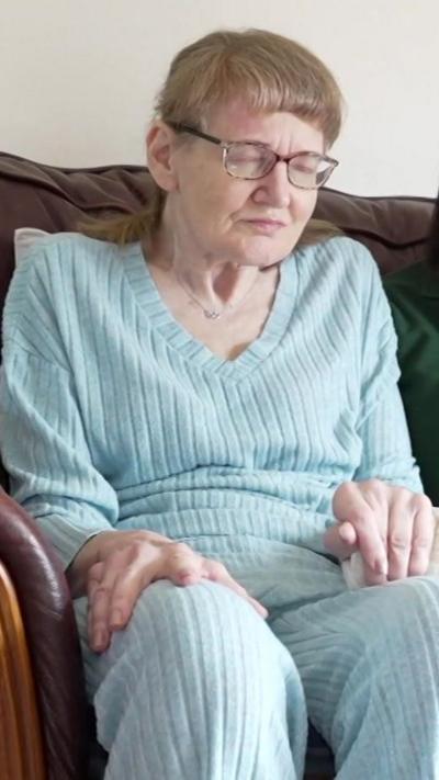 Woman in her 60s sitting on a sofa wearing a blue v-neck jumper