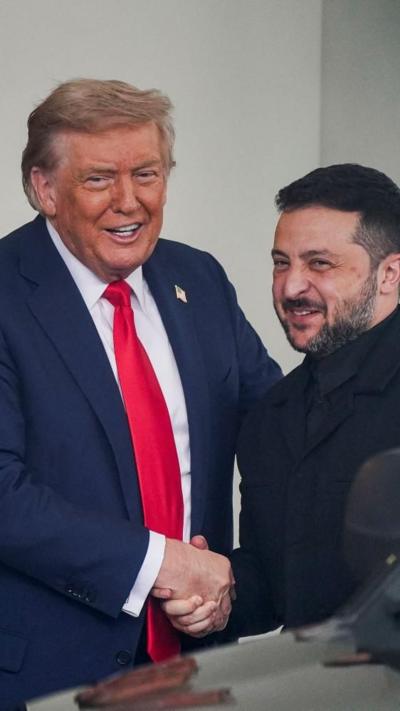 Trump shakes hands with Zelensky, both smiling, at the entrance of the White House