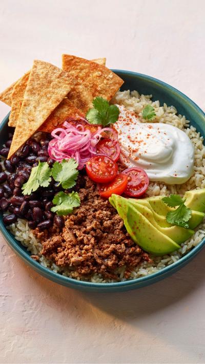 A green bowl with tortilla chips, mince, beans, rice and other taco ingredients in