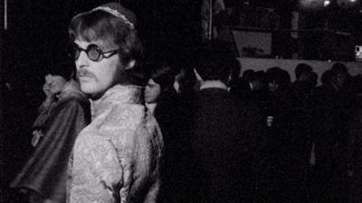 A man wearing round glasses in a nightclub.