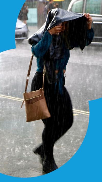 A woman holding her coat over her head while walking outside in the rain