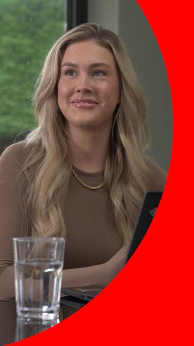 Blonde woman smiles looking to left of camera, in front of a glass of water. 