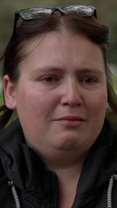 A close-up of Jasmine Beverley during an interview at a cemetery, with gravestones visible in the background.