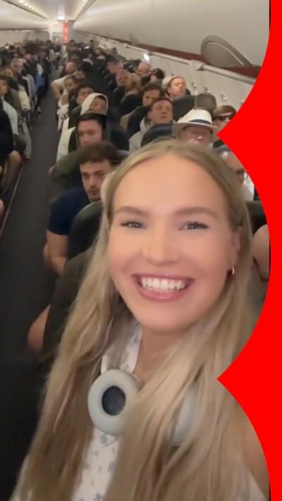 A woman smiling in the front row of a plane while other passengers look at her