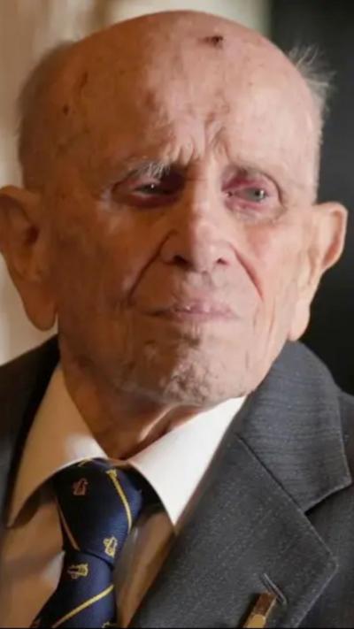 An elderly man is wearing a grey jacket and blue tie