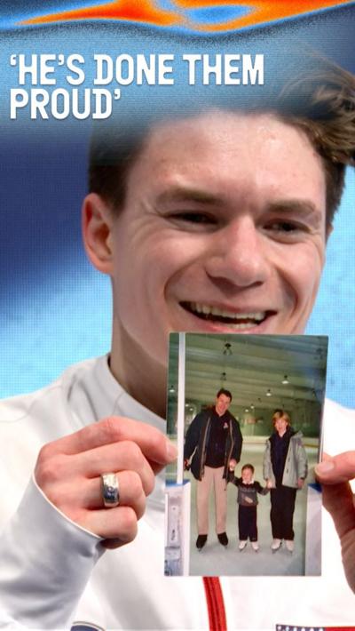 Maxim Naumov smiles as he holds up a photo of him as a child with his parents