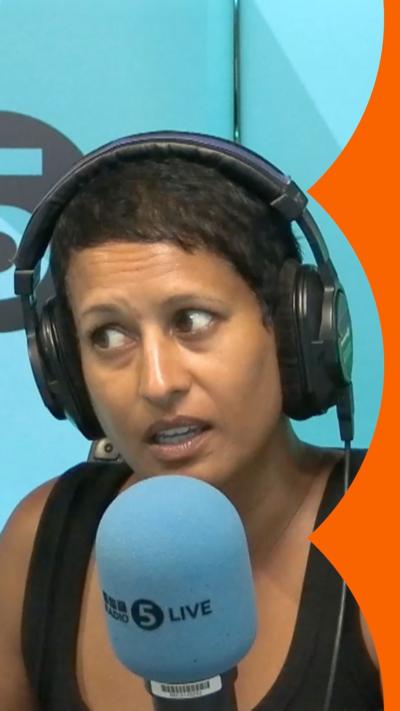 Naga Munchetty has short black hair. She is wearing a black vest top and is sitting behind a 5 Live microphone.
