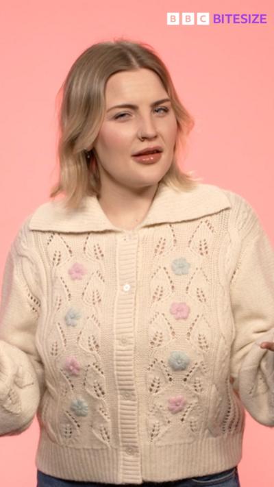 Mared Parry in a white cardigan with her arms outstretched in front of a pale pink background