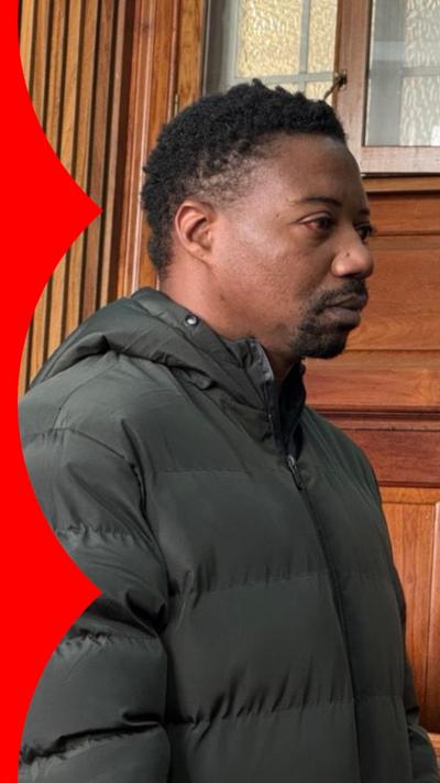 A man in a green puffer jacket with short dark hair and a short dark beard stands in court
