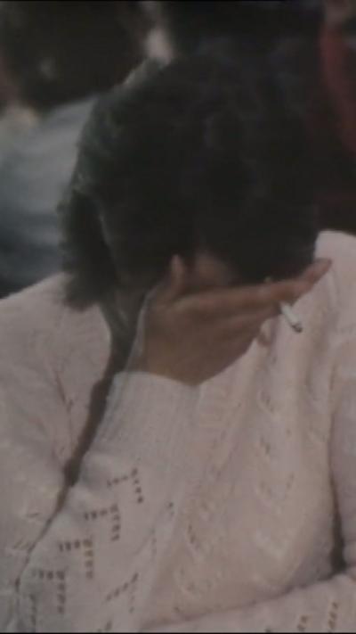 Woman in a white jumper with her head in her hand which is also holding a cigarette