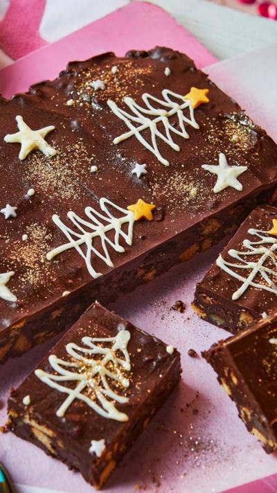 A Christmas pudding tiffin decorated with Christmas trees and stars, with three pieces cut off, sits on a pink tray
