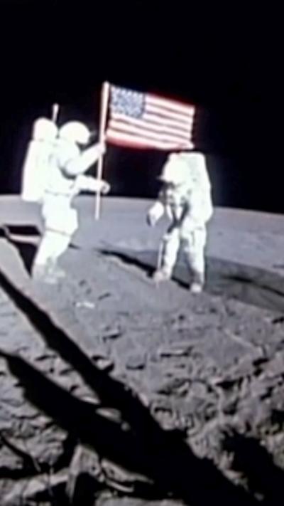 A low quality archive image of two astronauts walking on the moon, one holding a US flag